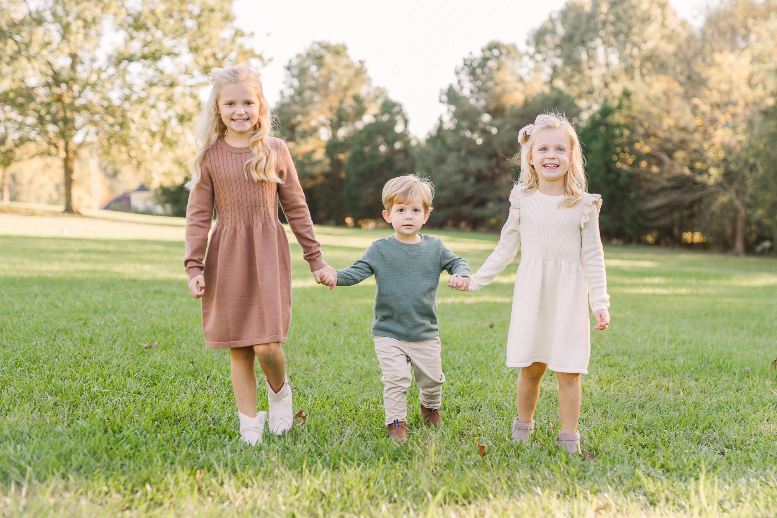 3 siblings holding hands and walking towards the camera, Joyful family during mini session guide in Madison, MS