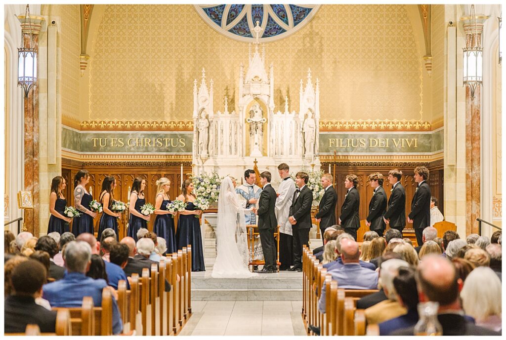 Anna and John Parker exchange vows surrounded by their bridal party and wedding guests at the Cathedral of St. Peter the Apostle in Jackson, Mississippi.