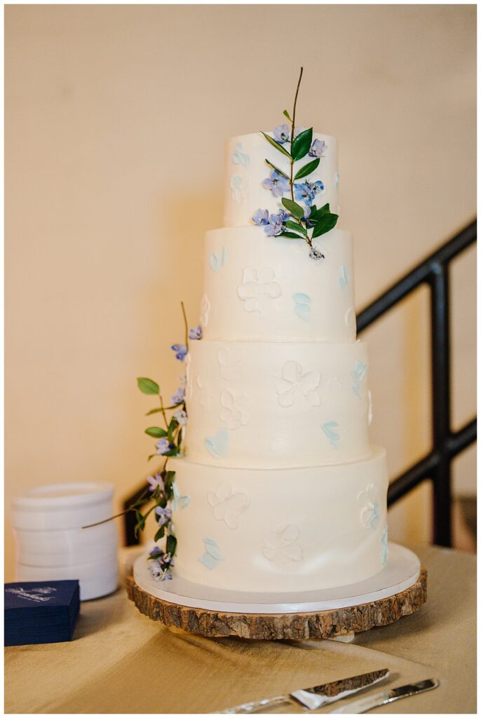 Wedding cake decorated with white flowers, blue and lavender flowers, and greenery at The Raymond Venue in Raymond, Mississippi.